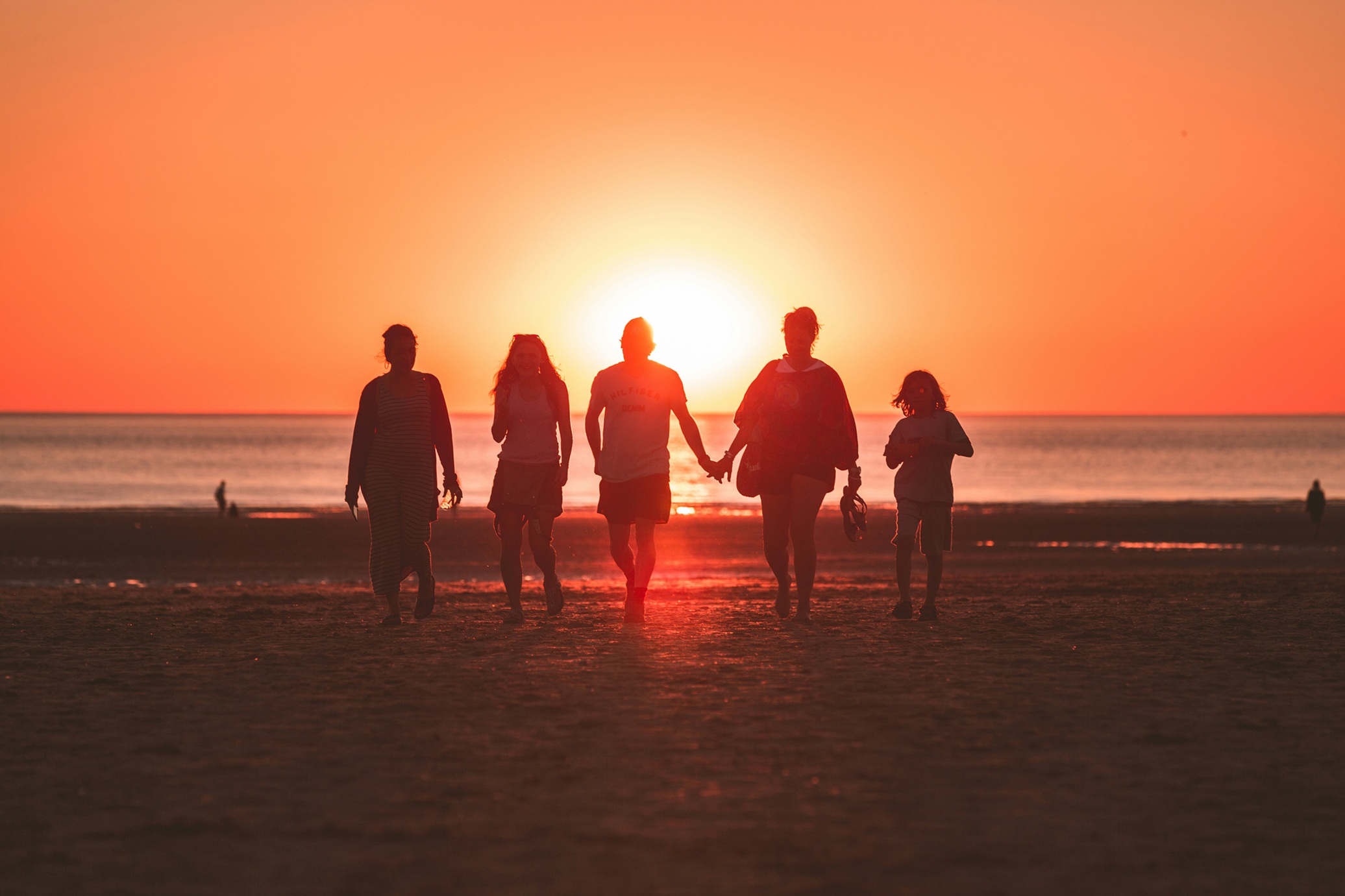 5 silhouettes of people of different ages walking on a beach, with a sunset in the background